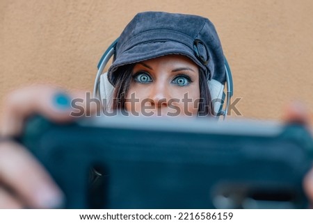 close-up of light-eyed woman with mobile phone and headphones playing or taking selfie
