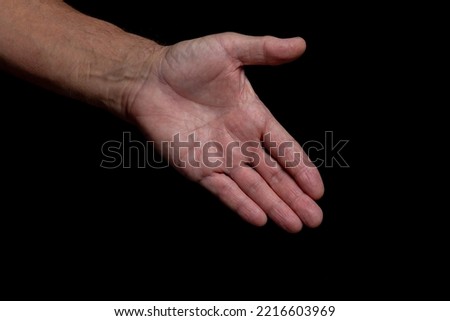The outstretched greeting hand of an elderly man, isolated on a black background. 