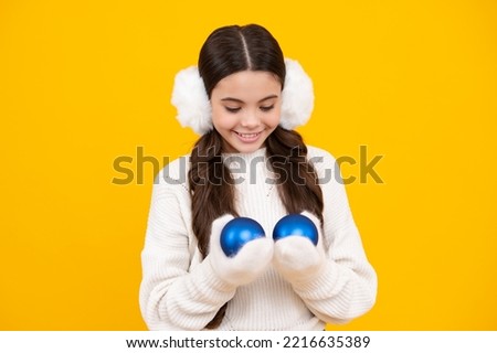 Portrait of happy teenager child wears sweater and knitted gloves on yellow isolated background. Kid in winter clothes. Teen girl with decorative christmas ball. Happy face, positive and smiling girl.