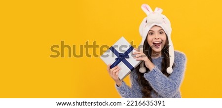 happy teen girl wear earflap hat holding purchase box on yellow background. Kid girl with gift, horizontal poster. Banner header with copy space.