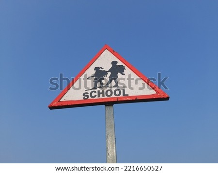 School sign plate in the roadside. Triangular school ahead sign plate near the road. Drive slow sign. School crossing sign in India. 
