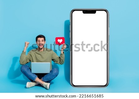 Full size photo of delighted man sit floor raise fist celebrate success isolated on blue color background