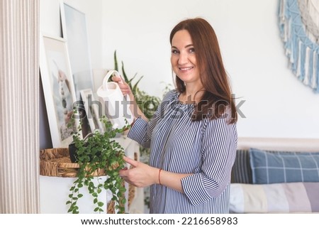 Cute housewife woman watering flowers from a stylish white minimalistic watering can. Lots of beautiful indoor plants