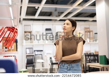 Young beautiful woman choosing the right chair furniture for her house at showroom. Female looking and thinking near lot of armchair at furniture store hall. Buying various item for new house Royalty-Free Stock Photo #2216672085
