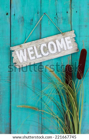 Wood welcome sign hanging on antique teal blue wooden fence with cattails border