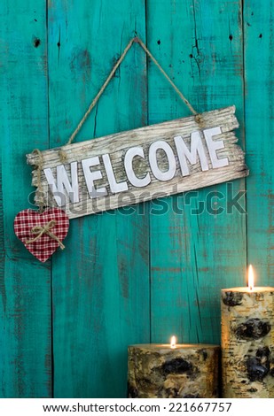 Wooden welcome sign with red heart and burning candles hanging on antique teal blue weathered fence