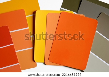 Color sample swatches scattered on a table. Swatches are in autumnal shades of yellows, oranges, reds and grays. Fall color schemes. Interior design color pallet.