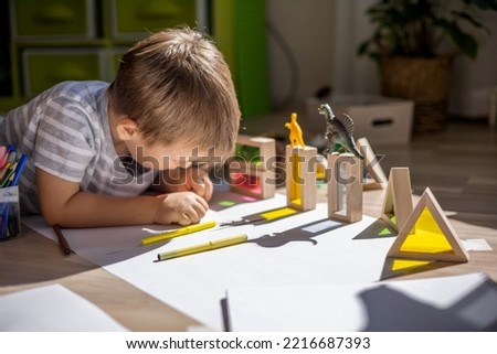 Male kid playing wooden bricks and dinosaurs drawing shadow on paper early development education. Preschooler creative idea handwriting painting picture contour animal figures detail with felt tip pen