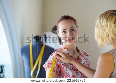 Young needlewoman taking measures of female client