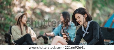 Selective focuse, beautiful Asian woman and friends travelers  relaxing at front of camping tent, They enjoy to talking and drinking beer with fun and happy together