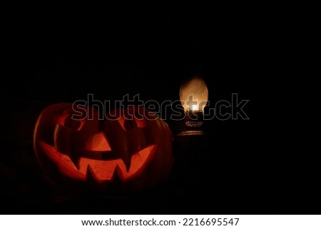 Festive pumpkin and lamp on a dark background. Halloween pumpkin silhouette with red light from inside and kerosene lamp glowing with natural light. Dark photo. Selective focus.