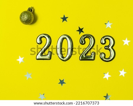 2023 on yellow background with copy space. Greeting card - happy new year with numbers 2023 on yellow background with small stars and golden christmas ball. Bright holiday concept. Top view. Flat lay