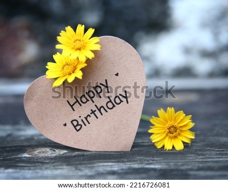 Happy Birthday text on paper card with flower decoration on wooden background