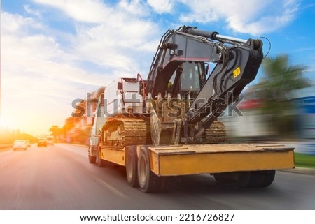 Transportation of a dirty excavator on a truck trailer after its work. Motion speed and blur effect on city highway, during sunset sky Royalty-Free Stock Photo #2216726827