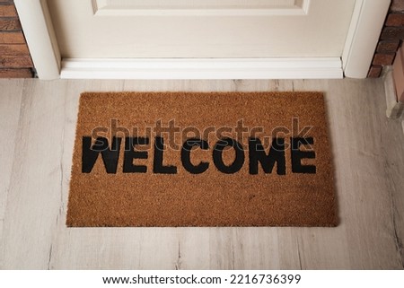 Door mat with word Welcome on wooden floor in hall, above view Royalty-Free Stock Photo #2216736399