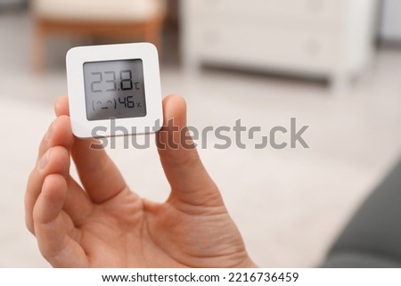 Woman holding digital hygrometer with thermometer at home, closeup. Space for text Royalty-Free Stock Photo #2216736459