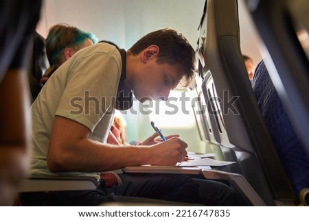 Tourist hand filling immigration form on flight to visit destination country sitting in airplane. Man is writing entry permit or visa on a paper on a flight. Passenger signing document on board.