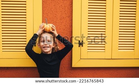 Cute little girl holding small pumpkin on the orange background. Halloween or thanksgiving celebration.