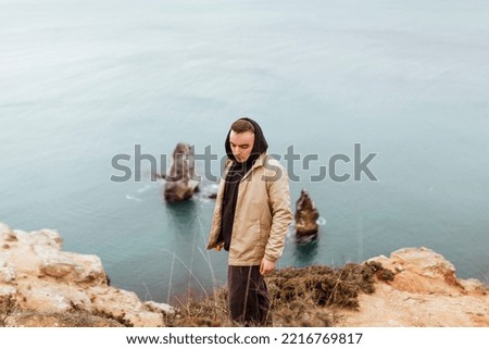A young man in a hood is sad and looks at the stunning mountain and sea landscape