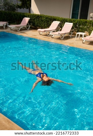 Woman in blue swimsuit swimming on the back in the pool during hot sunny day