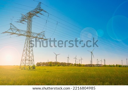 Beautiful farm landscape and industrial high voltage power line pylons and wind turbines farm at sunset warm colors and direct sun light with lens flare and sun rays in Germany Royalty-Free Stock Photo #2216804985