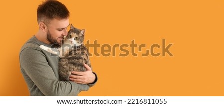 Young man and cute cat on orange background with space for text