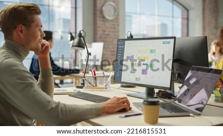 Portrait of White Creative Young Man With Glasses Working on a Computer During Day Time in a Spacious Modern Office. Male Graphic Designer Smiling While Developing a New Visual Concept for Website.