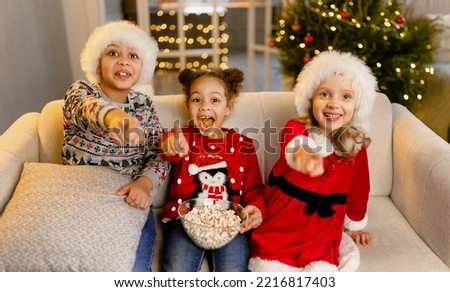 A children in Santa hats watch movies at home with popcorn on Christmas day pointing at the screen