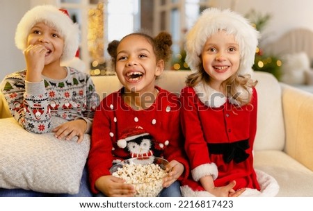 A children in Santa hats watch movies at home with popcorn on Christmas day pointing at the screen