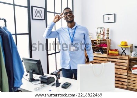 Young man working as manager at retail boutique doing peace symbol with fingers over face, smiling cheerful showing victory 