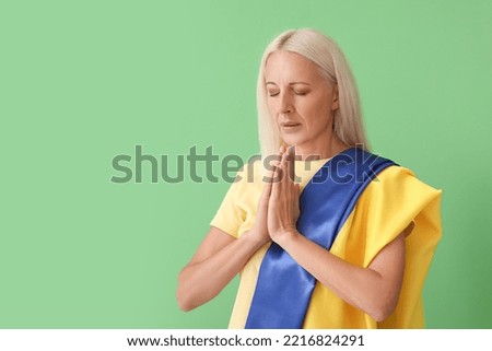 Mature woman with flag of Ukraine praying on green background