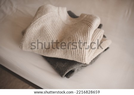 Stack of knitted wool textile sweaters clothes on white blanket in bed at home room close up. Winter cozy season. 