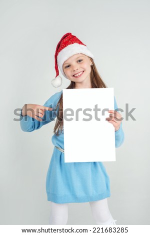 Cute girl in Santa Claus hat with a white blank paper sheet. Christmas, x-mas, New Year, Winter, people, advertisement, sale concept.
