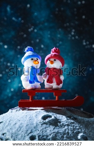 Two cute plasticine snowmen with sleds on the moon. Christmas card.