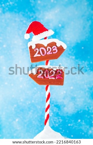 Wooden 2023 and 2022 direction signs and santa hat on blue background. In anticipation of the New Year 2023.