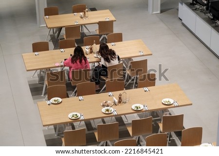 From above of females sitting at table in office canteen with served plates and silverware for employees and having meal Royalty-Free Stock Photo #2216845421