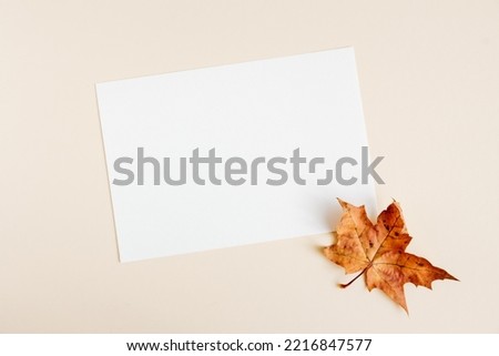 Invitation card mockup with autumn maple tree leaves on beige pastel background. Template blank of white paper mock up for branding and advertising. Top view, flat lay, copy space.