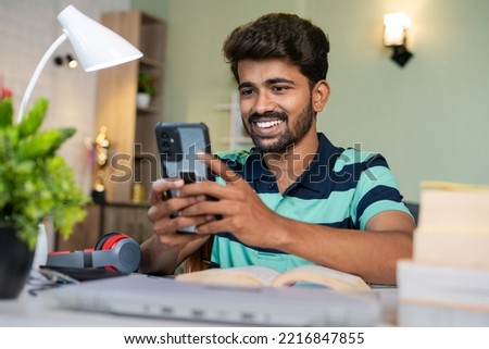 happy smiling college Student using mobile phone while reading at study desk - concept of relaxation, taking break and social media addiction