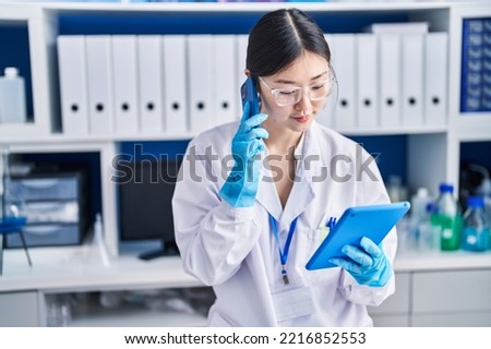 Chinese woman scientist using touchpad talking on smartphone at laboratory