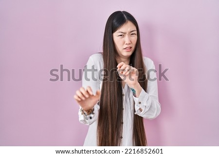 Chinese young woman standing over pink background disgusted expression, displeased and fearful doing disgust face because aversion reaction.  Royalty-Free Stock Photo #2216852601