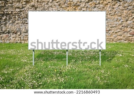 Blank advertising signboard in a green mowed lawn of a public park against an old stone wall - concept  with copy space and space for inserting text.