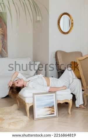 A woman is lying on a sofa in a stylish, bright living room next to a beautiful picture she painted herself