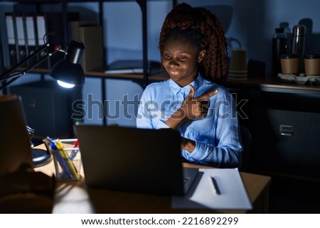 African woman working at the office at night cheerful with a smile of face pointing with hand and finger up to the side with happy and natural expression on face 