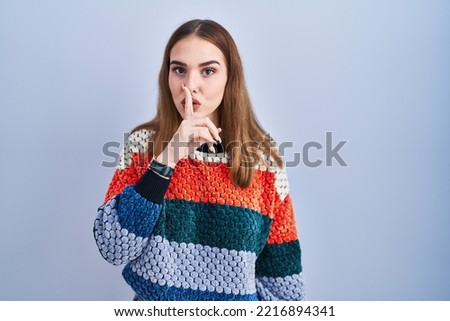 Young hispanic girl standing over blue background asking to be quiet with finger on lips. silence and secret concept. 