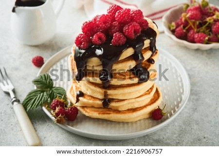 American pancakes. Stack pancakes with fresh raspberry with chocolate glaze or toppings in white bowl on light gray table background. Homemade classic american pancakes. Magazine concept. Top view.
