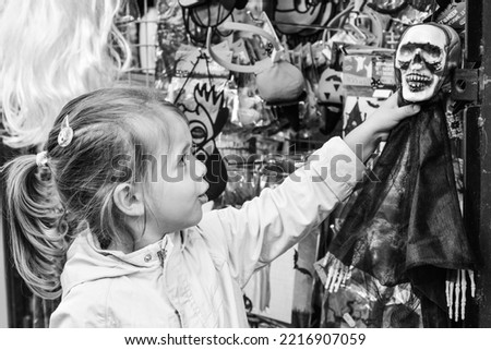Cute little girl grabbing a skeleton in front of the shop during Halloween celebrations - Halloween business concept and consumerism concept - Black and white