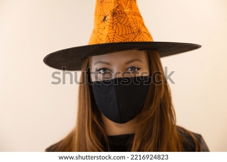 Halloween, a girl in a medical mask and a witch costume. Only the eyes are visible. Pandemic on Halloween
