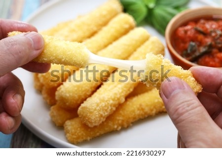 Breaking freshly fried mozzarella sticks and stretching cheese with both hands. Royalty-Free Stock Photo #2216930297