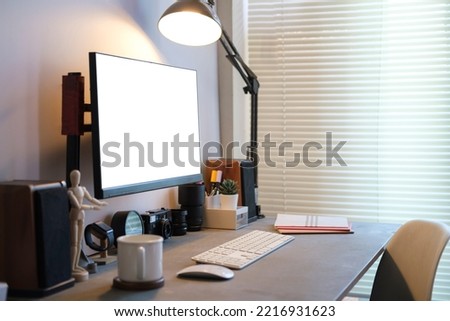 Creative workplace with white blank computer screen,lamp and supplies on black wooden table.
