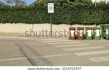 Priority to pedestrian and cyclists, warning road sign on concrete sidewalk. Concrete fence with hedge on behind, public recycle garbage bins and asphalt street in front. Background for copy space.